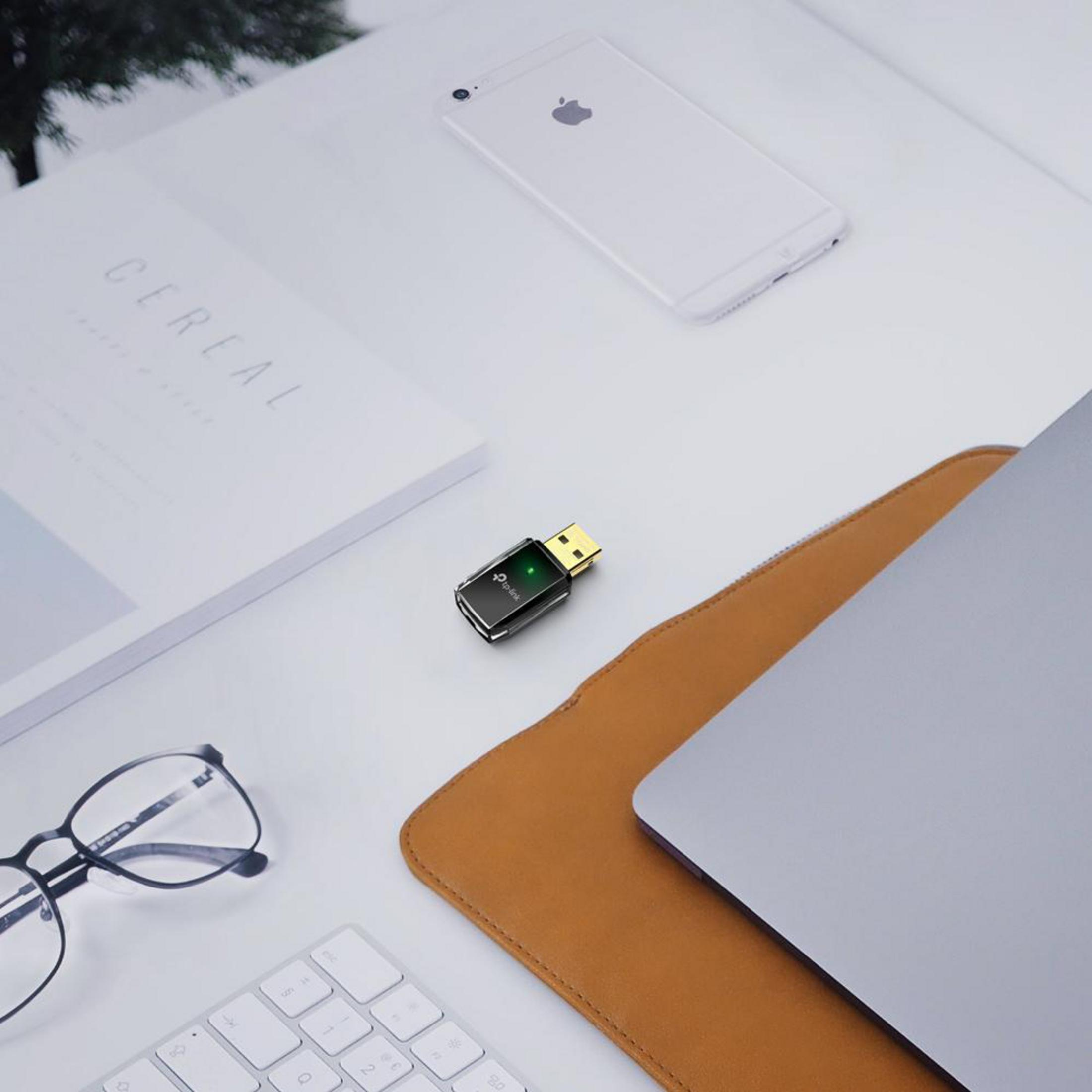 USB-WLAN-Adapter, Apple-Telefon, offenes Magazin, Brille, Tastatur und Laptop.