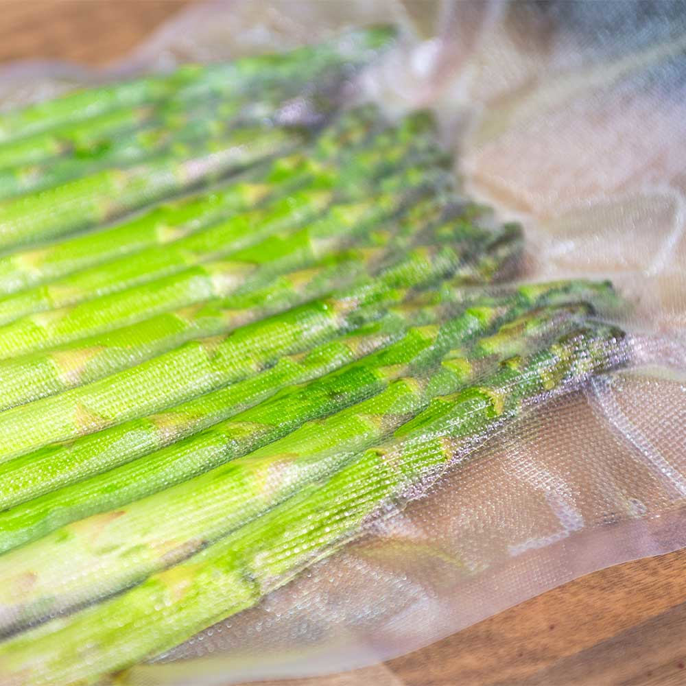 Punte di asparagi in un sacchetto di plastica sigillato, su una superficie di legno.