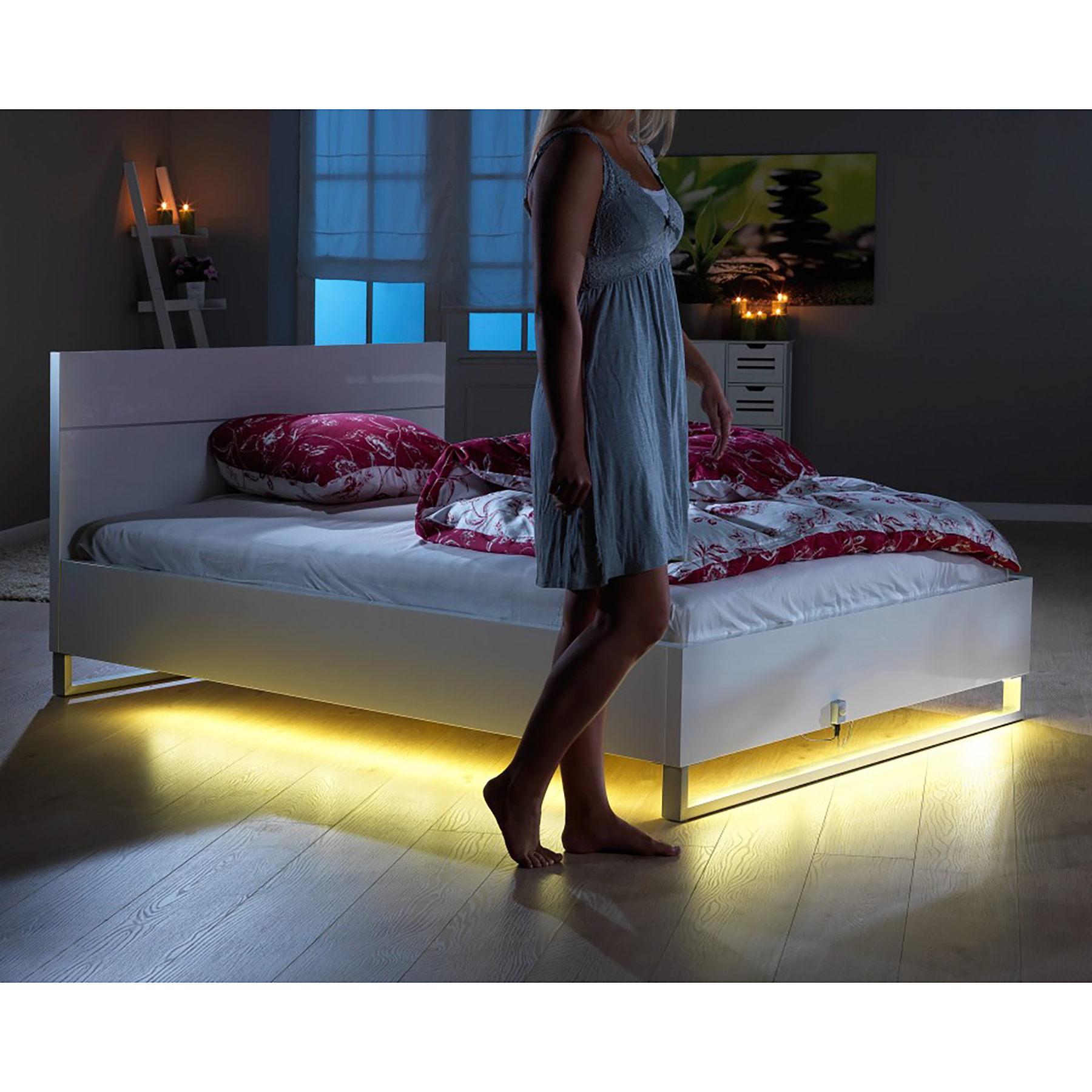 Eine Frau steht neben einem Bett, das Bett hat Unterbettlichter.