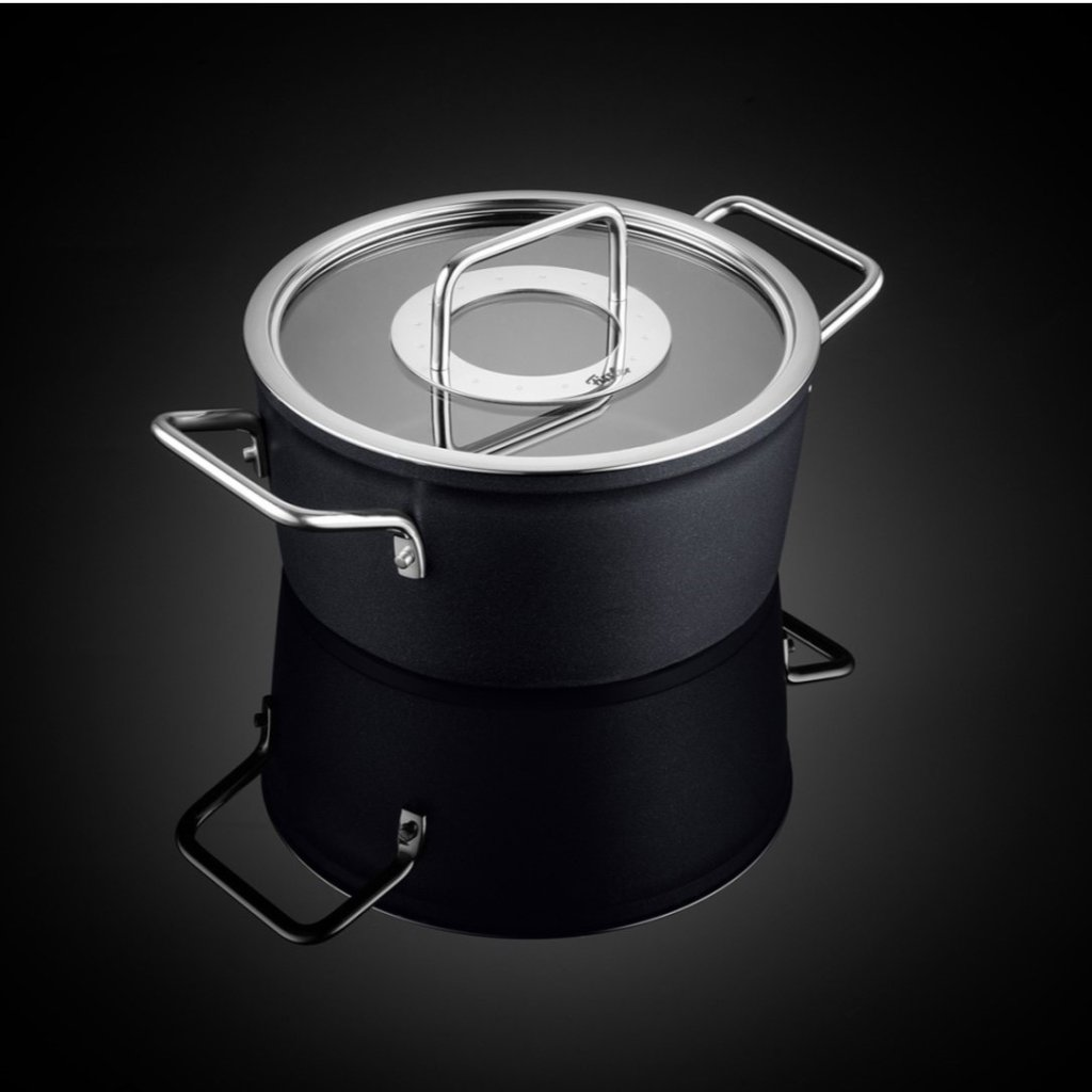 Czarny garnek ze szklaną pokrywką i dwoma uchwytami, na odbijającej czarnej powierzchni.