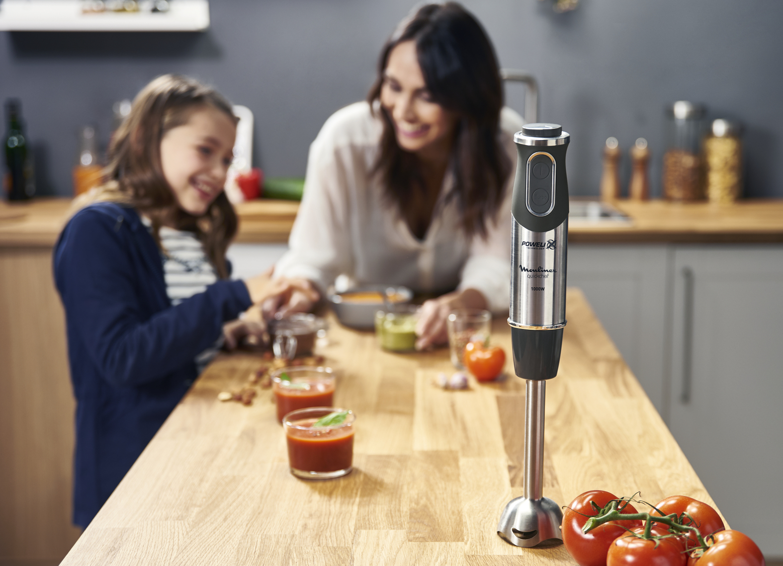 Kobieta i dziewczynka przygotowują jedzenie blenderem ręcznym na drewnianym blacie kuchennym.