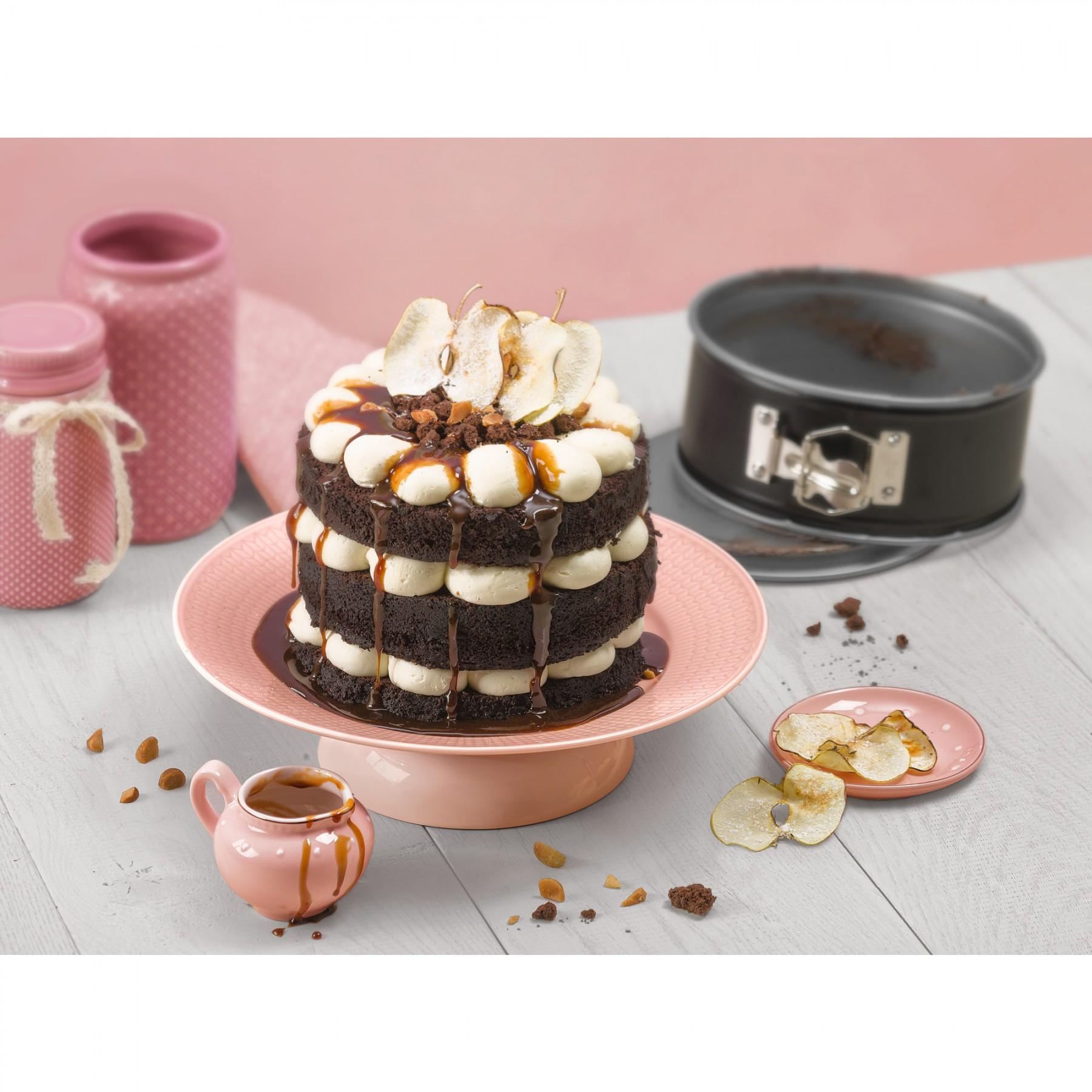 Warstwowe ciasto czekoladowe z sosem karmelowym, kremem i plasterkami gruszki na różowym stojaku.
