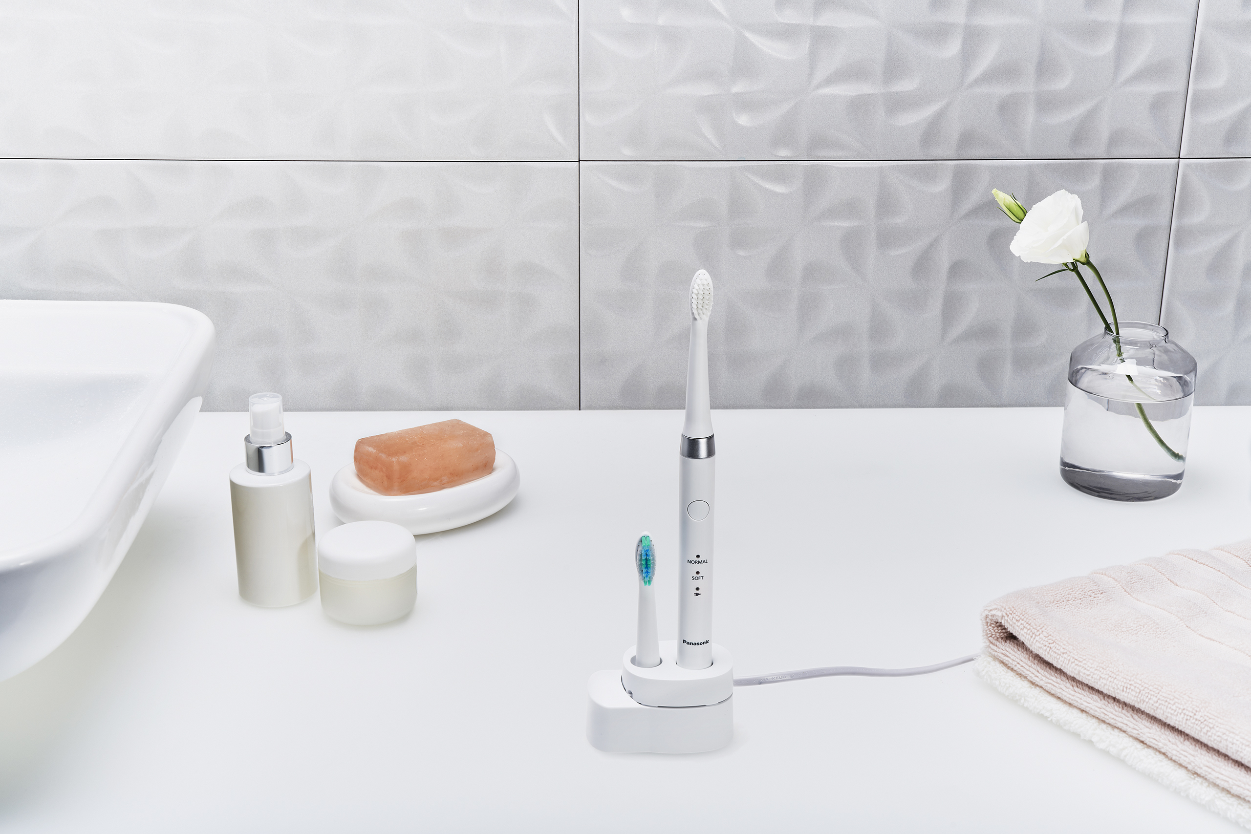 Scena łazienkowa z białym blatem, umywalką i szczoteczką do zębów. Obecne są także mydelniczka i wazon.