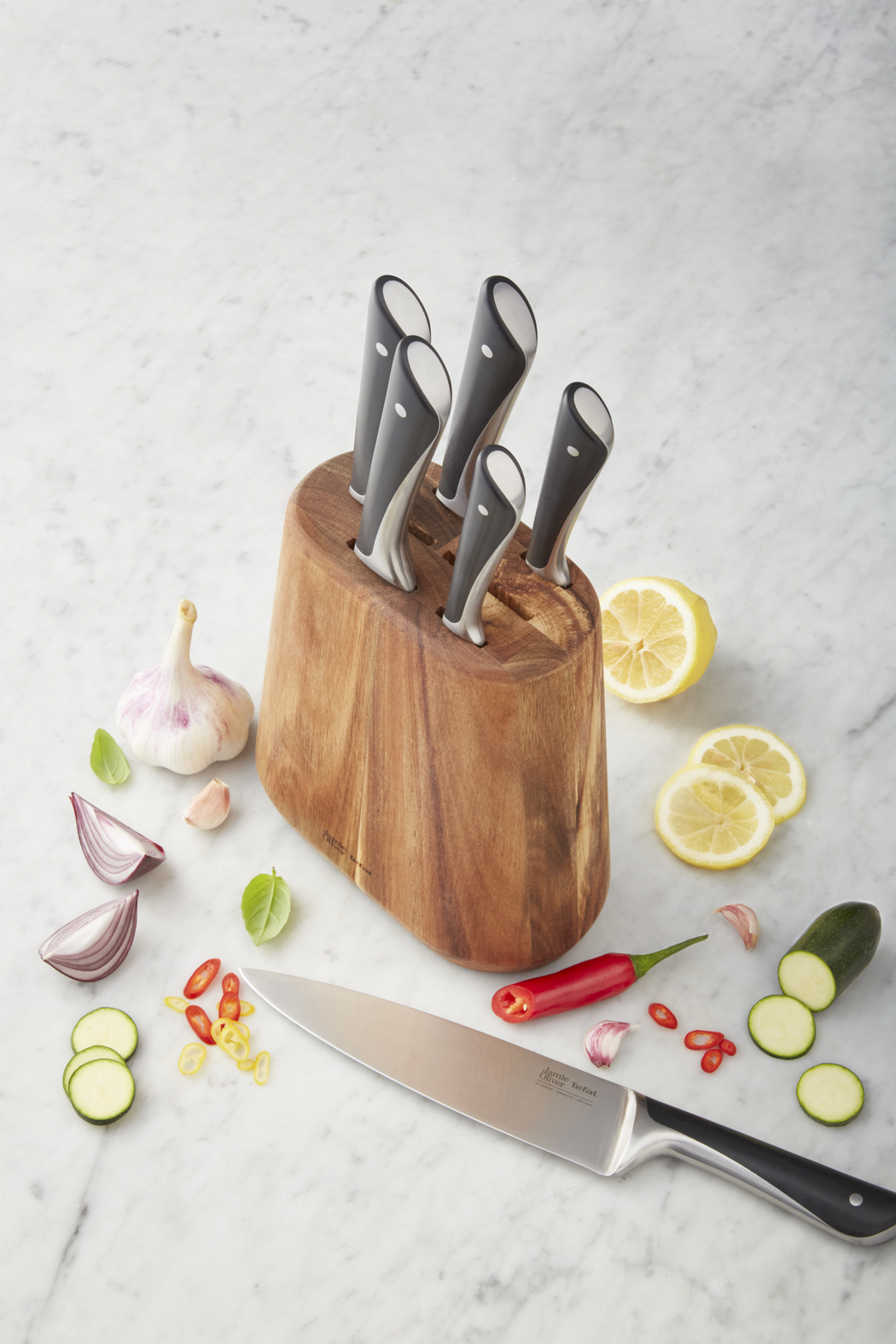 Un ceppo di legno con coltelli. Presenti anche aglio, fette di limone, peperoncino rosso e fette di zucchine.