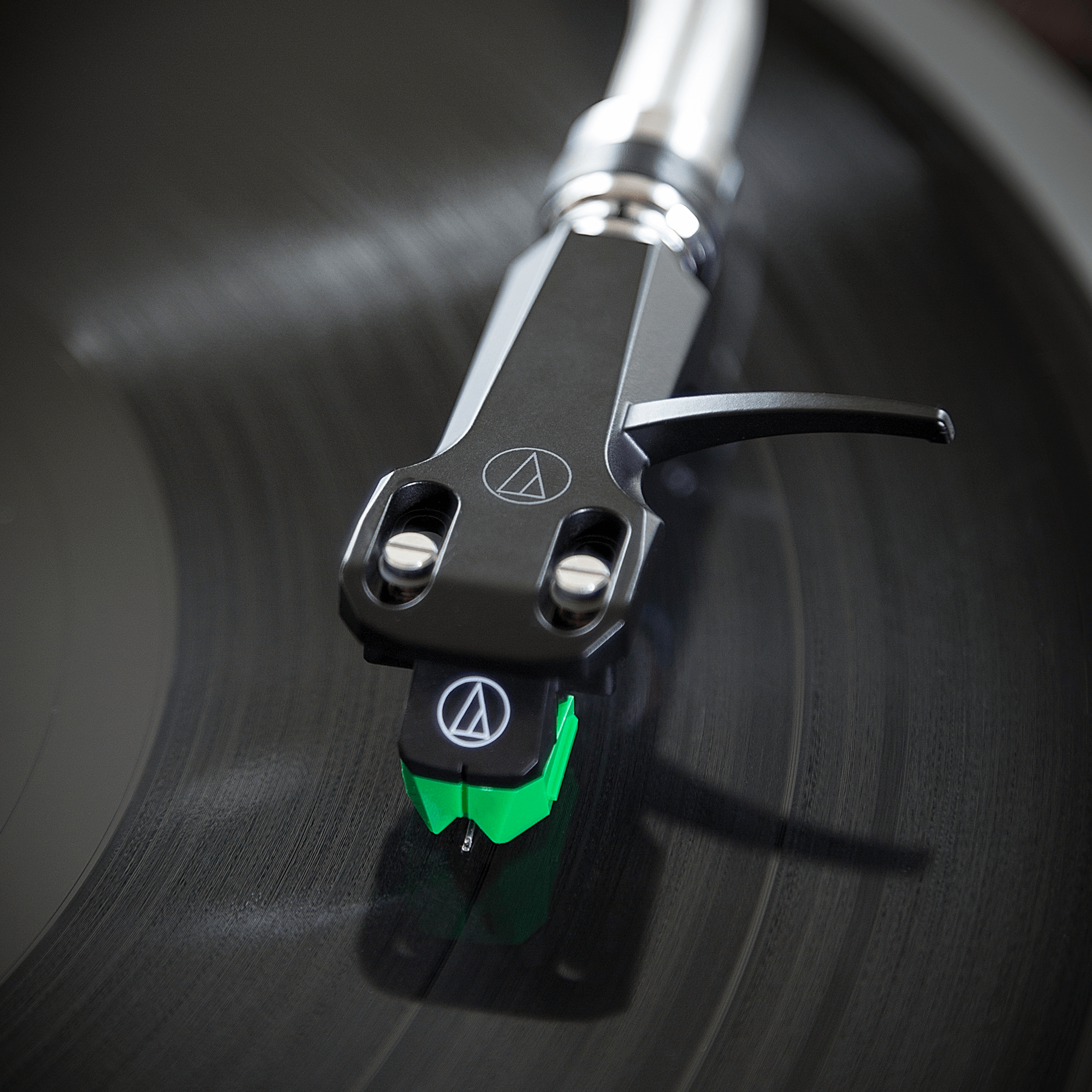 Nahaufnahme der Plattenspielernadel. Schwarze und grüne Details. Vinyl-Schallplatte spielt. Dunkler Hintergrund.
