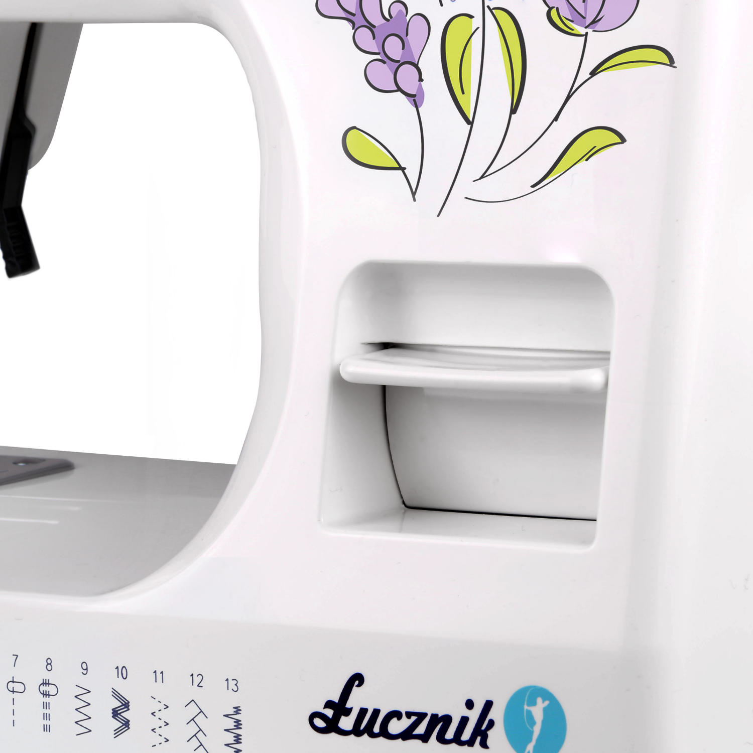 Zbliżenie białej maszyny do szycia z kwiatowym wzorem i logo Lucznik na białej powierzchni.