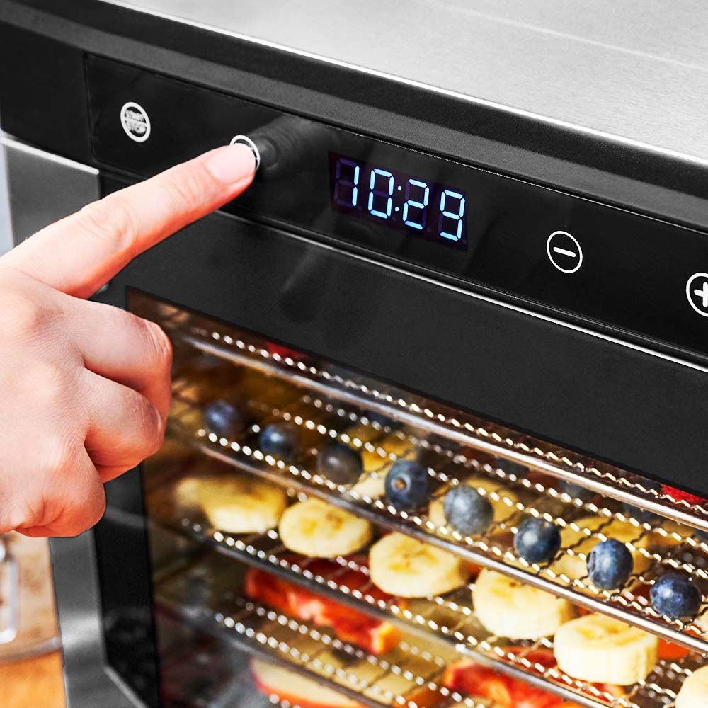Una mano preme un pulsante su un essiccatore, mostrando l'ora. Frutta a fette è visibile all'interno.