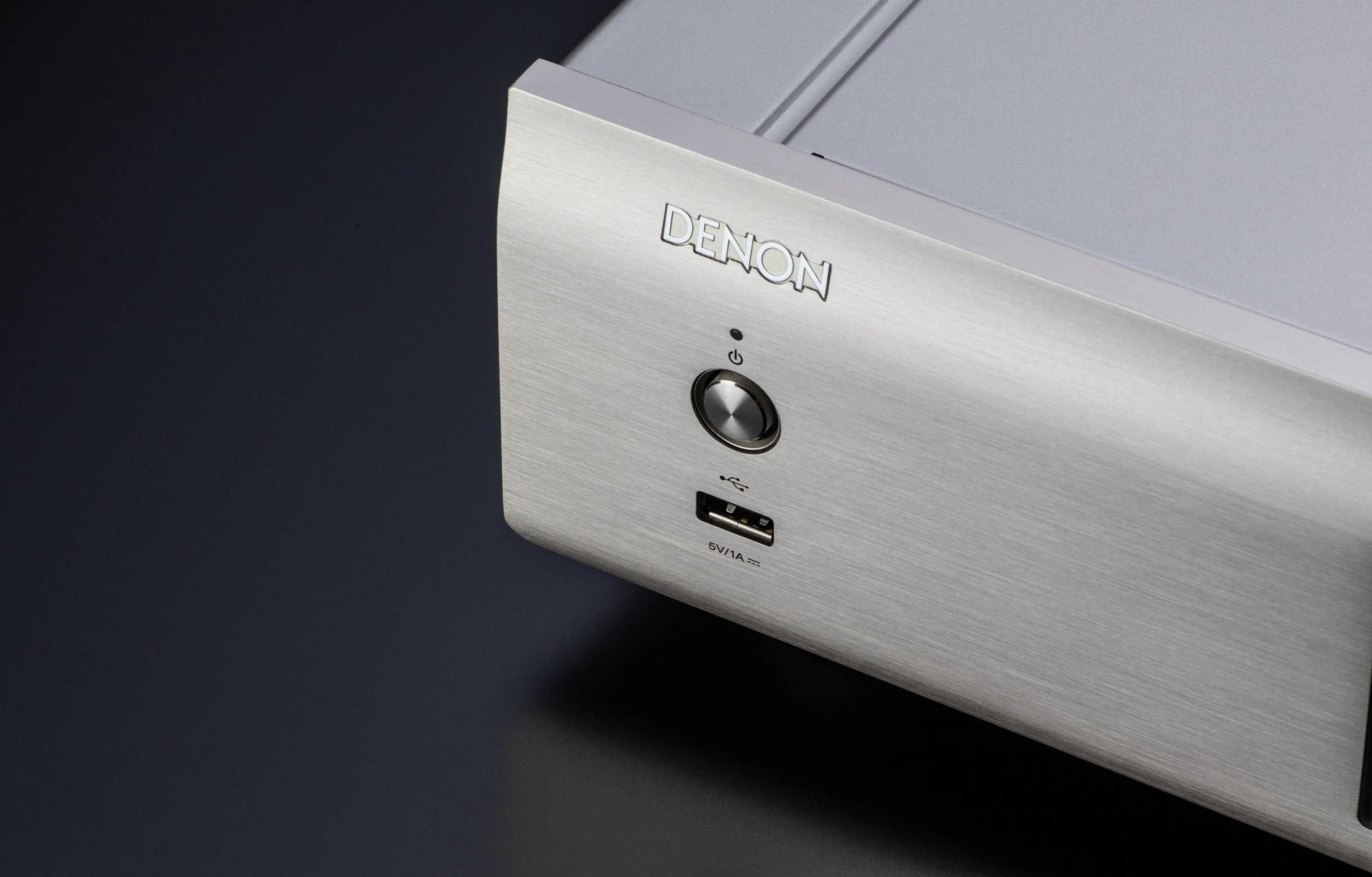 Ein silberner Audio-Receiver mit Ein-/Aus-Schalter, USB-Anschluss und dem Denon-Logo wird angezeigt.