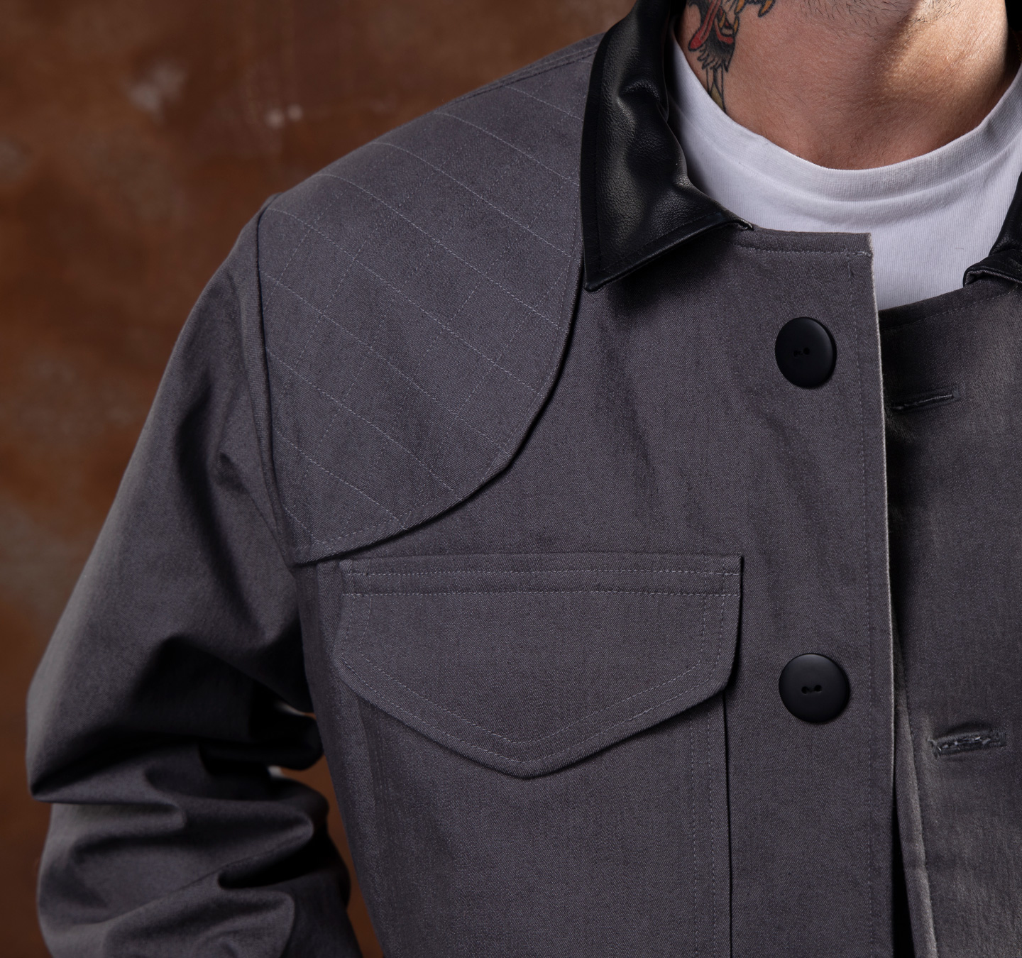 Zbliżenie szarej kurtki z czarnym kołnierzem i guzikami, noszonej przez mężczyznę.
