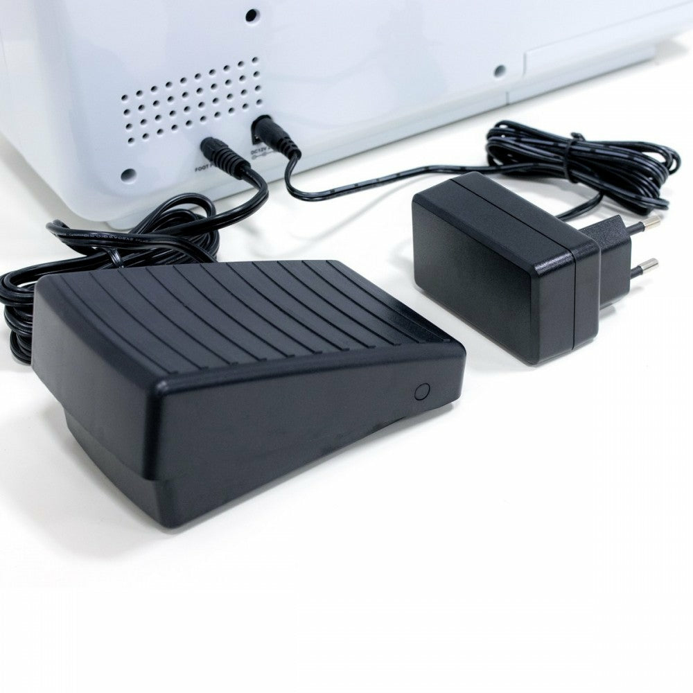Un pedal negro, un adaptador de corriente negro y una máquina blanca con cables.