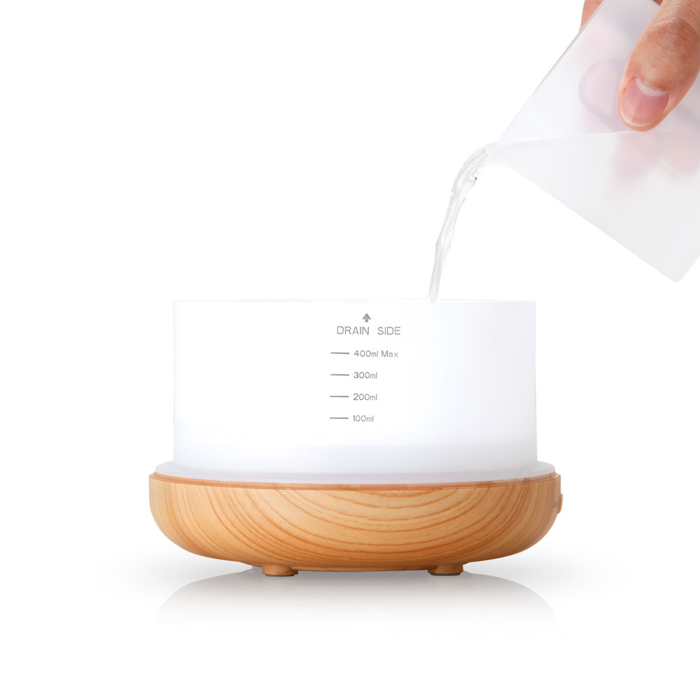 Osoba wlewa wodę do białego i drewnianego dyfuzora zapachowego.