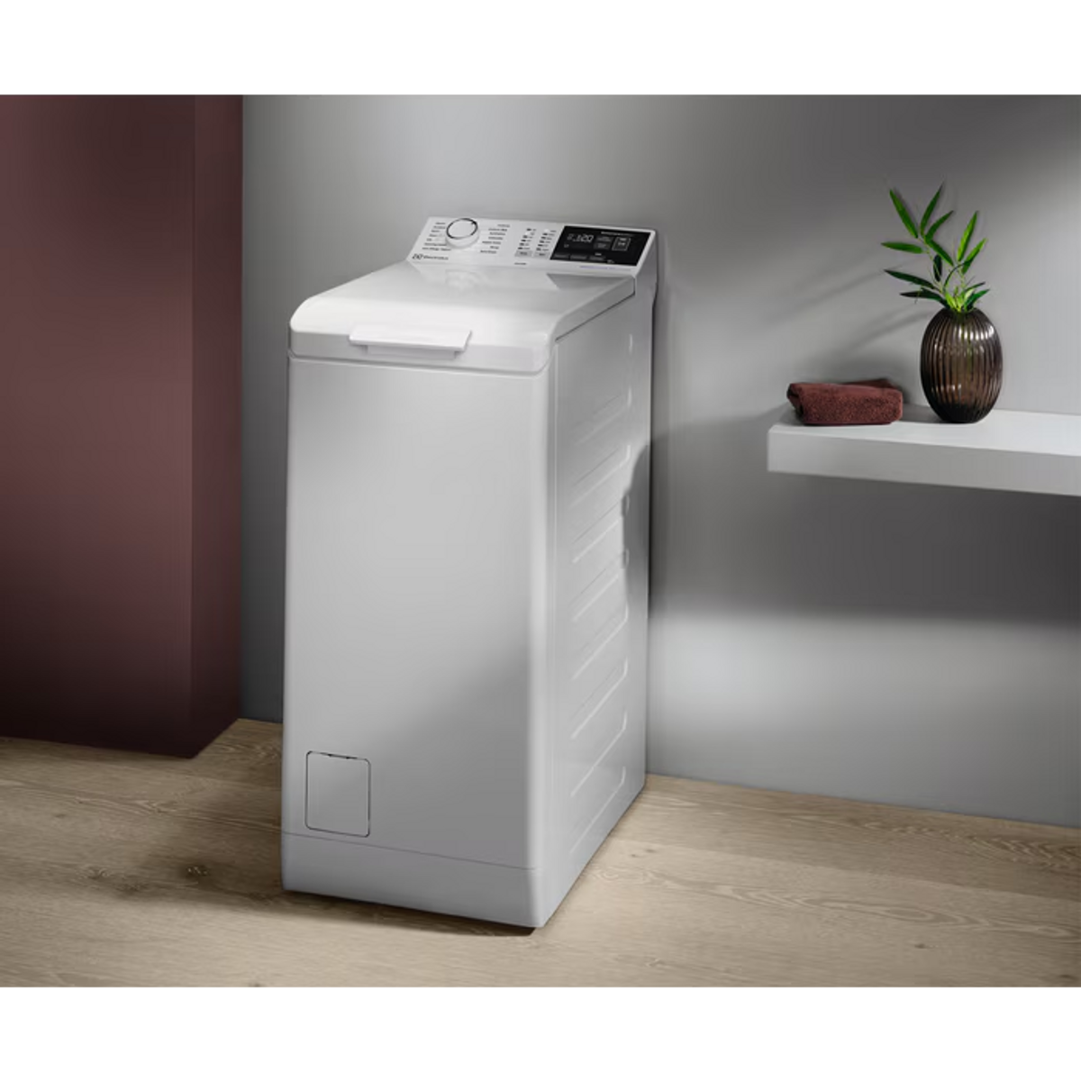 Biała pralka w pokoju. Jest półka z wazonem i ręcznikiem.