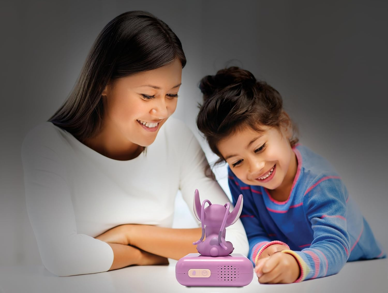Une femme et un enfant sourient et regardent une figurine Stitch sur un socle. L'arrière-plan est flou.