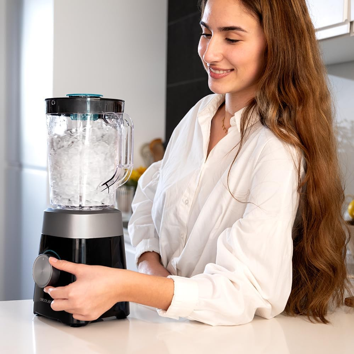 Eine Frau lächelt, während sie einen schwarzen und silbernen Mixer bedient.