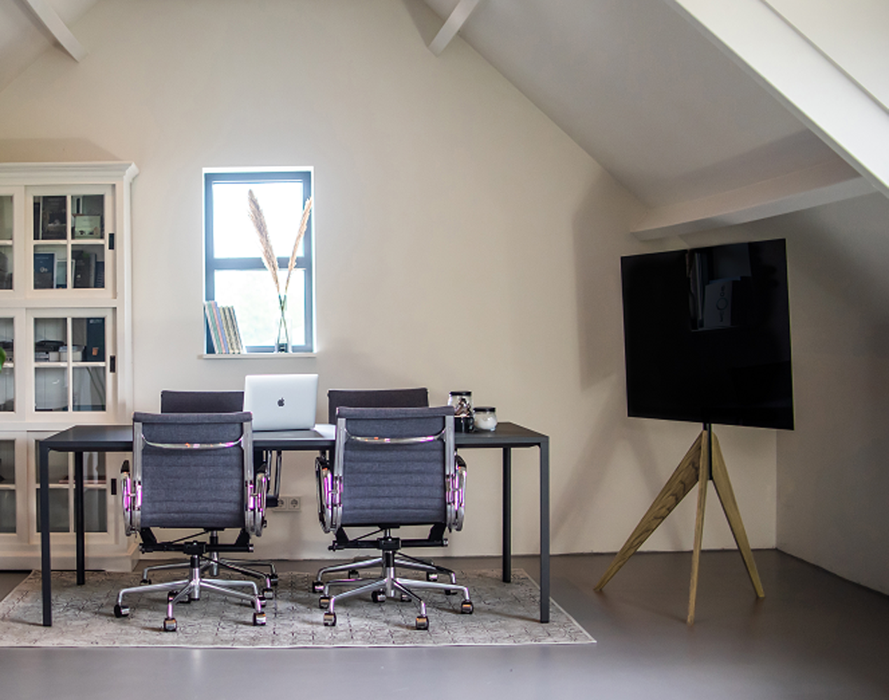Een kamer met een bureau, twee stoelen, een raam, een tv, een kast en een tapijt op de vloer.