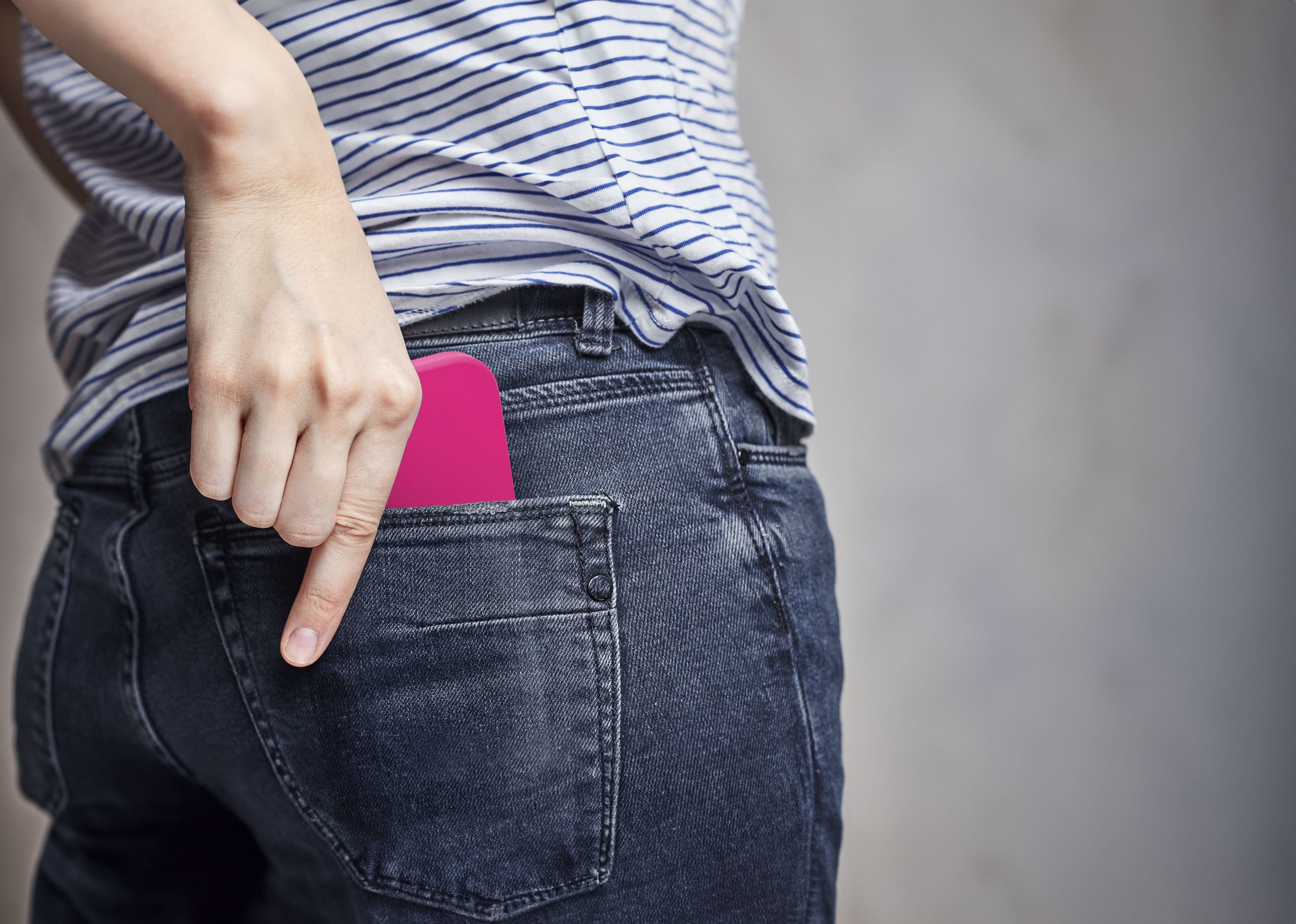 Una mano che raggiunge una tasca contenente un telefono rosa, con jeans.