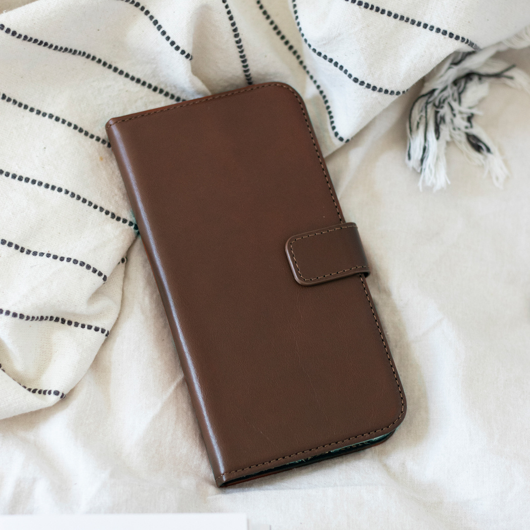 Bruine leren telefoonhoes met een knoopsluiting op een witte doek.