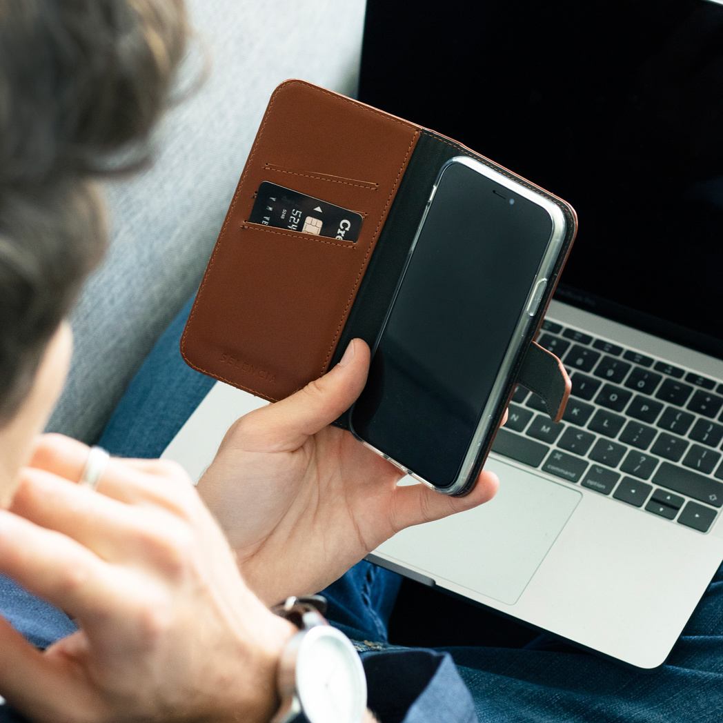 Eine Person hält ein Telefon in einer braunen Hülle neben einem Laptop mit Kreditkarte.