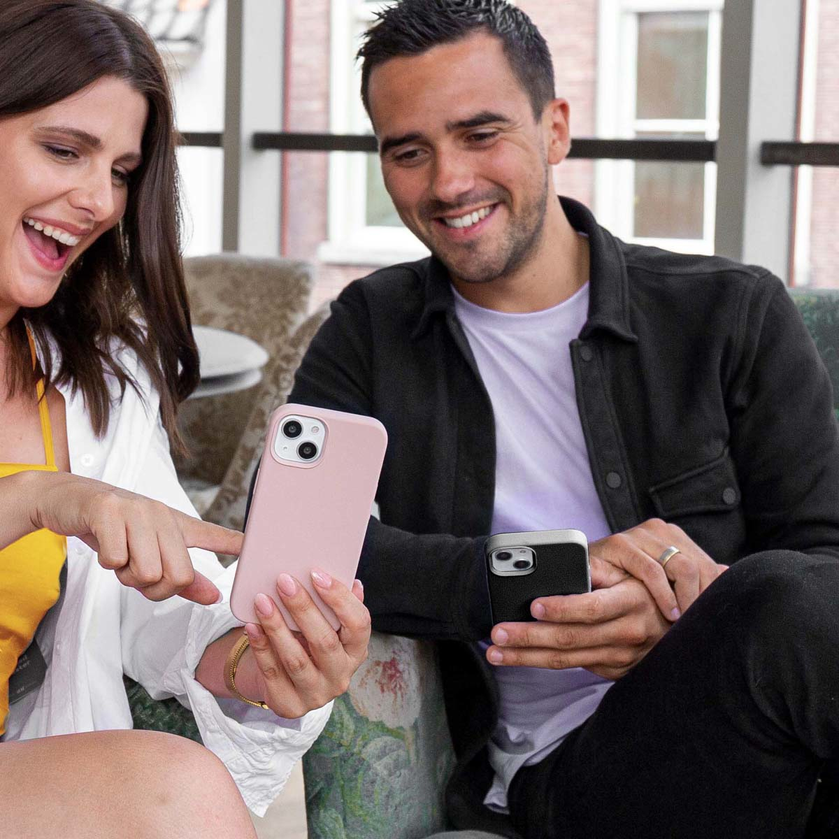 Zwei Personen betrachten Telefone mit Hüllen. Eine Person zeigt. Rosa und schwarze Hüllen.