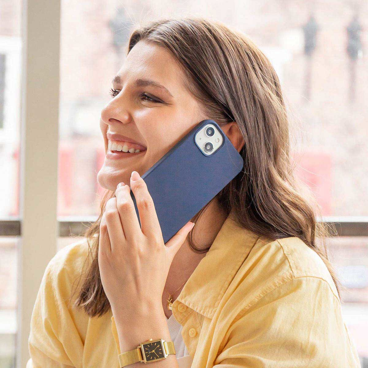 Een vrouw lacht en houdt een telefoon in een blauwe hoes aan haar oor.