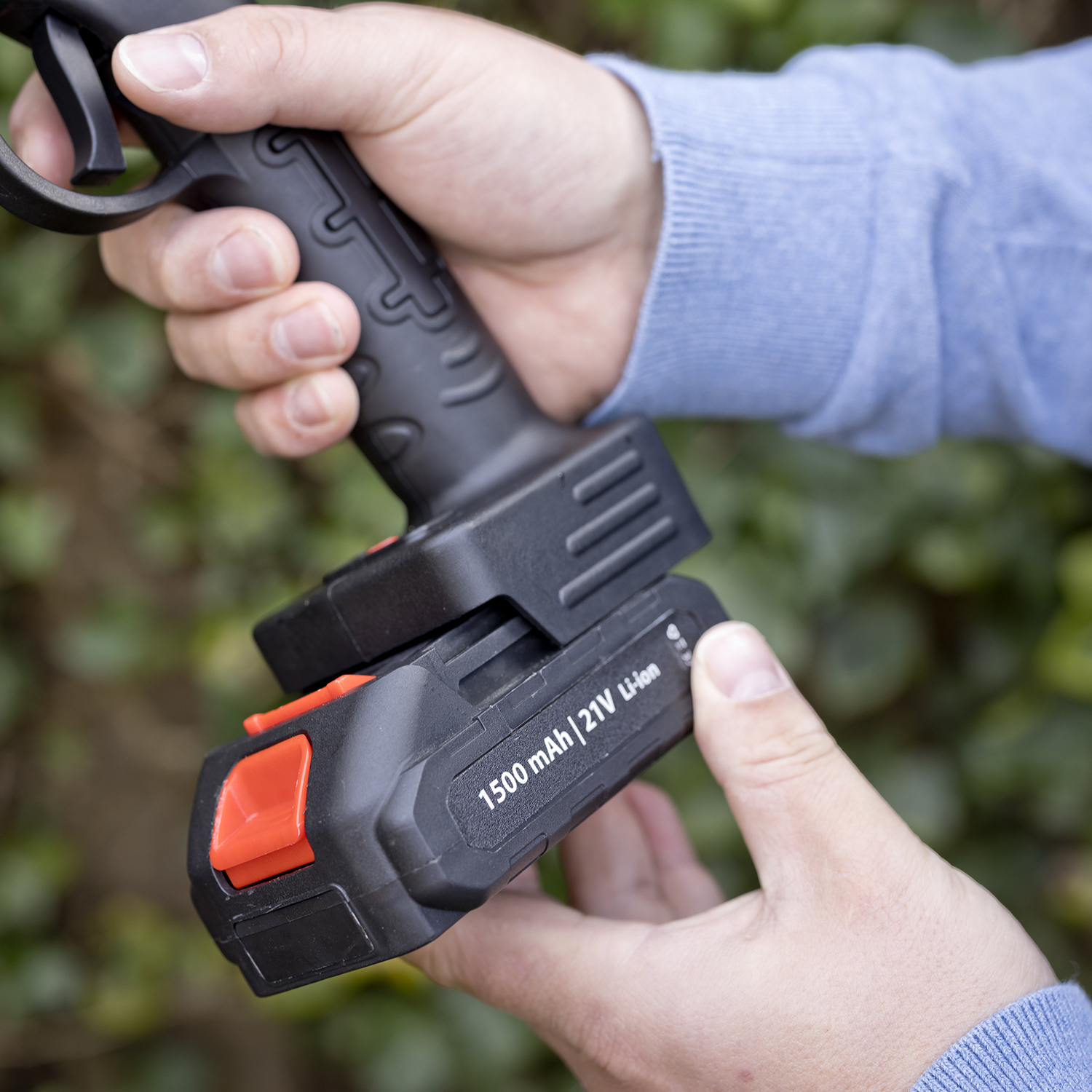 Handen installeren een 21V Li-ion batterij in een zwart elektrisch gereedschap. Batterij is gelabeld '1500 mAh'.
