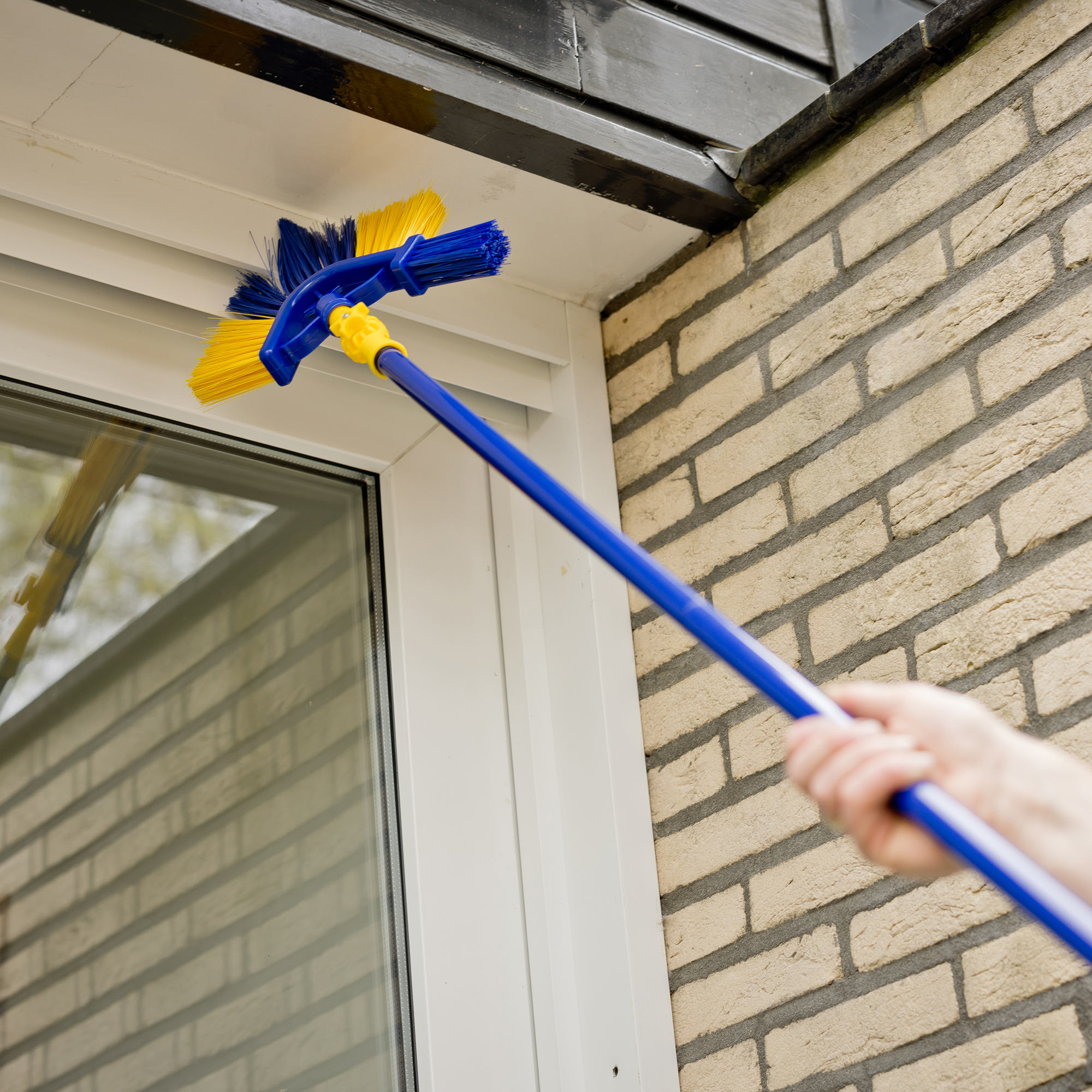 Een persoon maakt een kozijn schoon met een blauw-gele borstel.