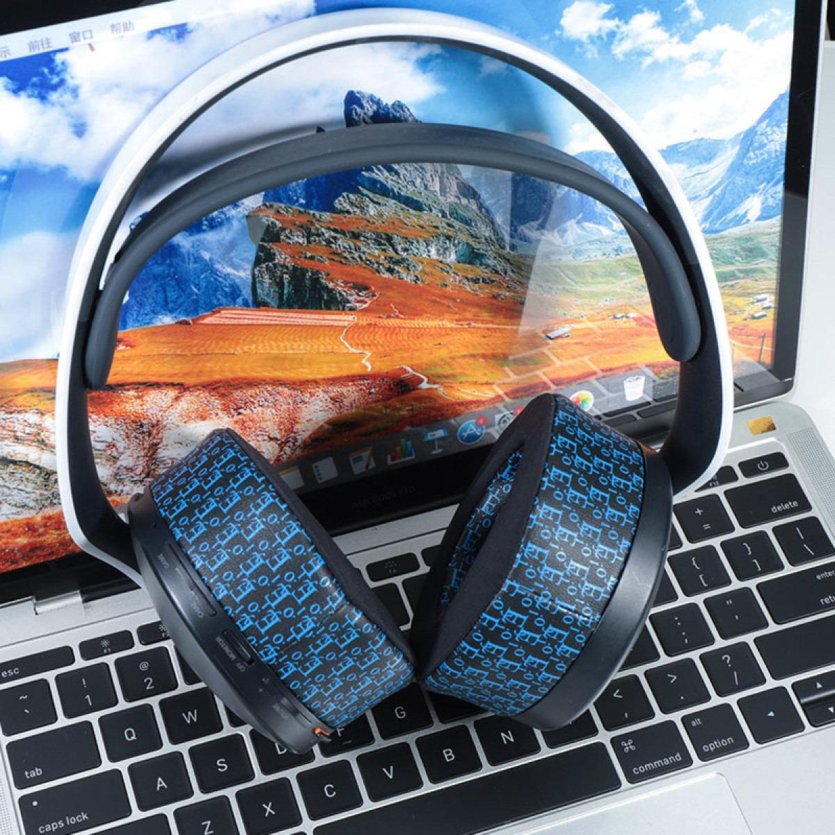 Kopfhörer auf Laptop, schwarz-weißes Design. Bildschirm zeigt Landschaft. Tastatur sichtbar.