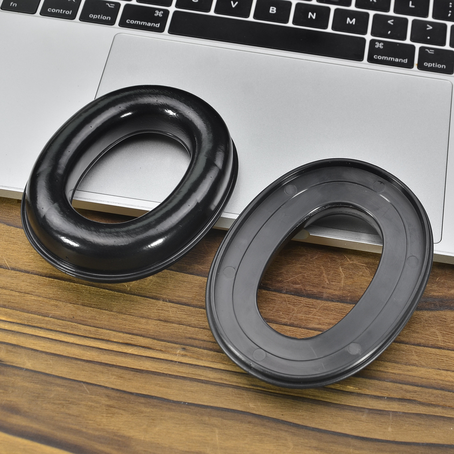 Due cuscinetti auricolari neri per cuffie e tastiera di un laptop su una superficie in legno.