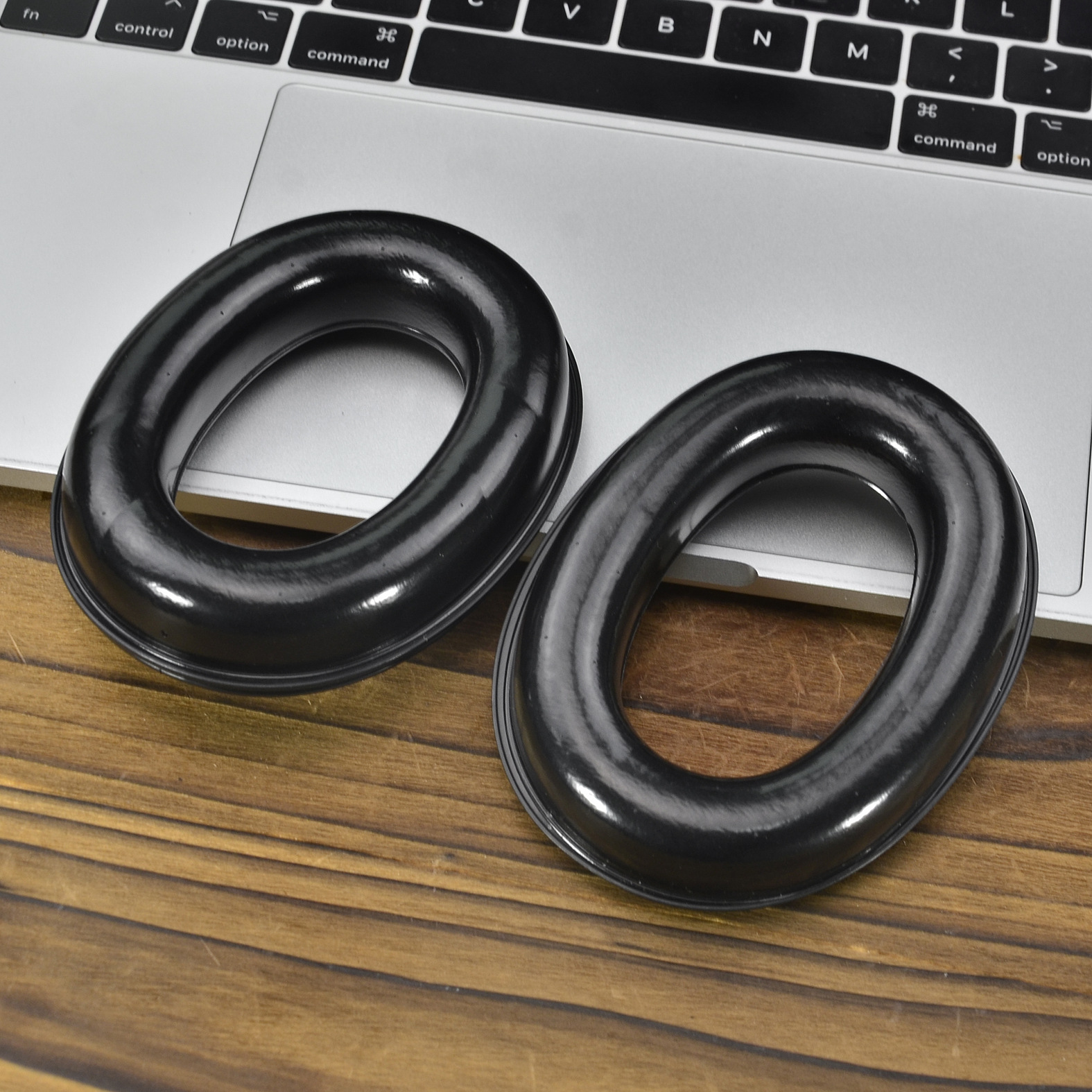 Due protezioni auricolari ovali nere per la riduzione del rumore sono su un tavolo, vicino a un laptop.