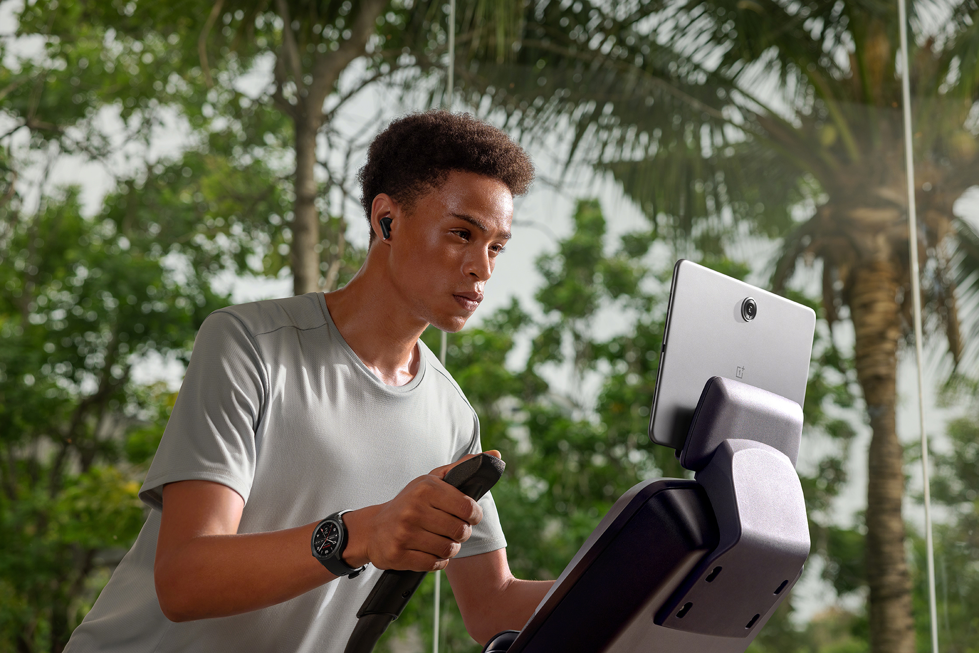 Mężczyzna na bieżni z tabletem i słuchawkami, ze słonecznym widokiem na zewnątrz.