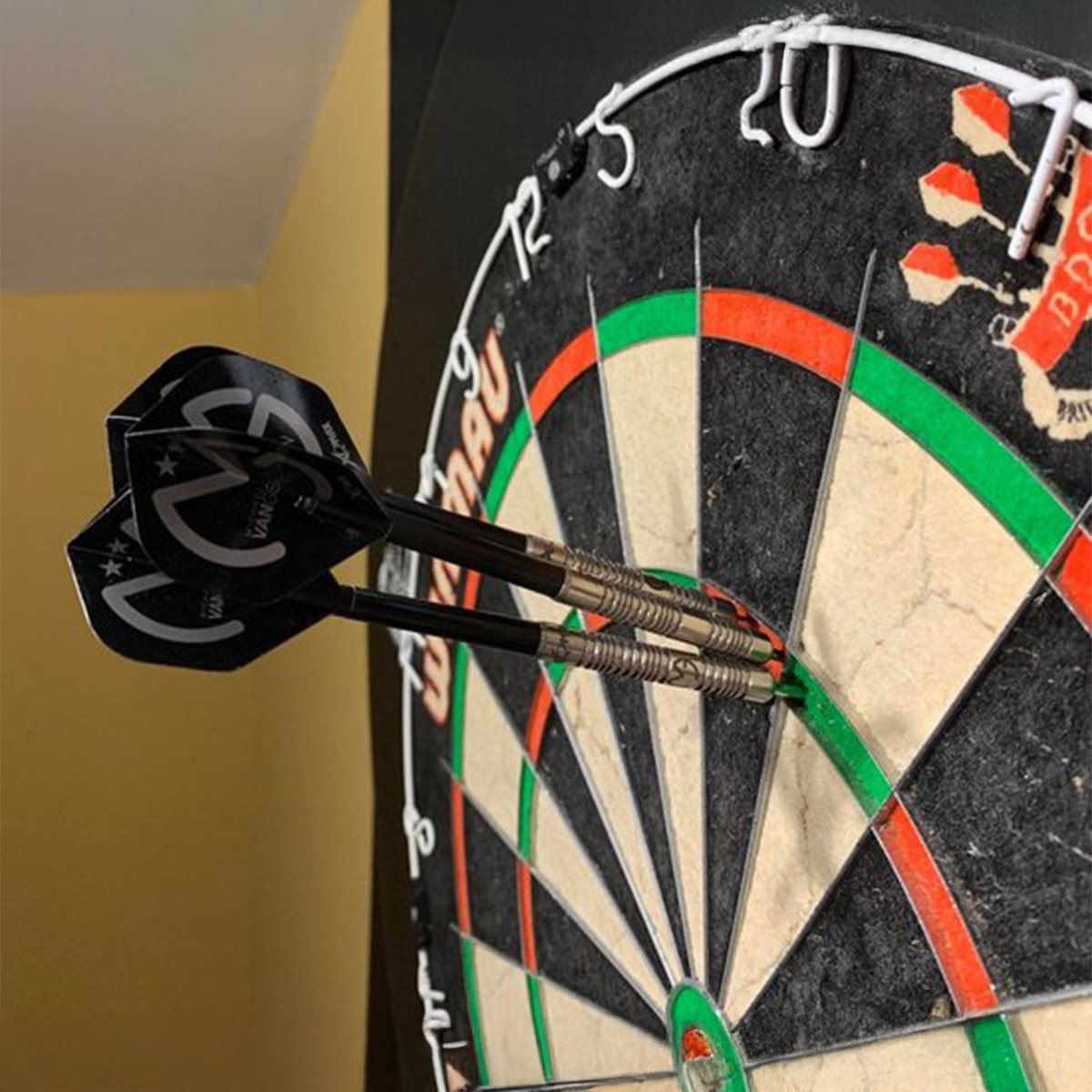 Drie darts in een dartbord. De darts zijn zwart en zilver. Het dartbord is zwart en rood.
