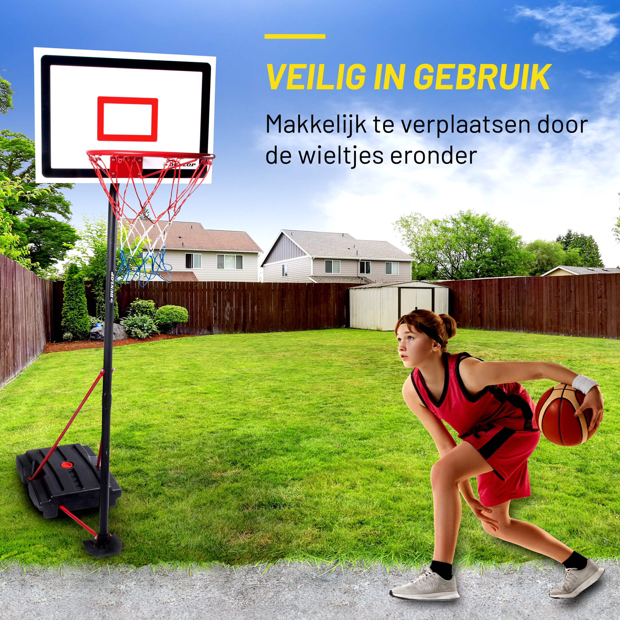 Meisje gooit een basketbal naar een basketbalring. Groen gazon, huizen op de achtergrond, blauwe lucht.