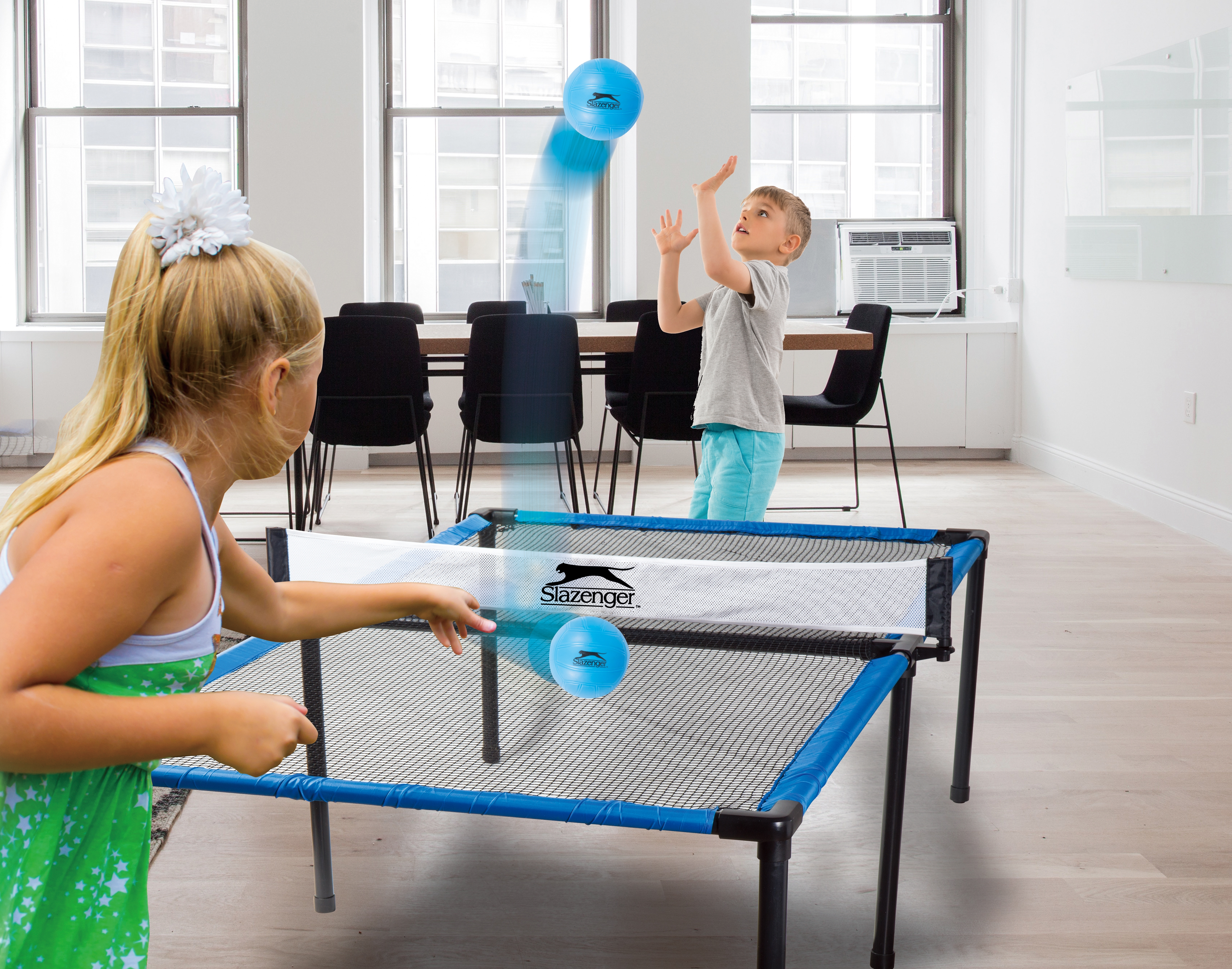 Twee kinderen spelen tafeltennis. Eén serveert een blauwe bal over het net. Binnenscène.