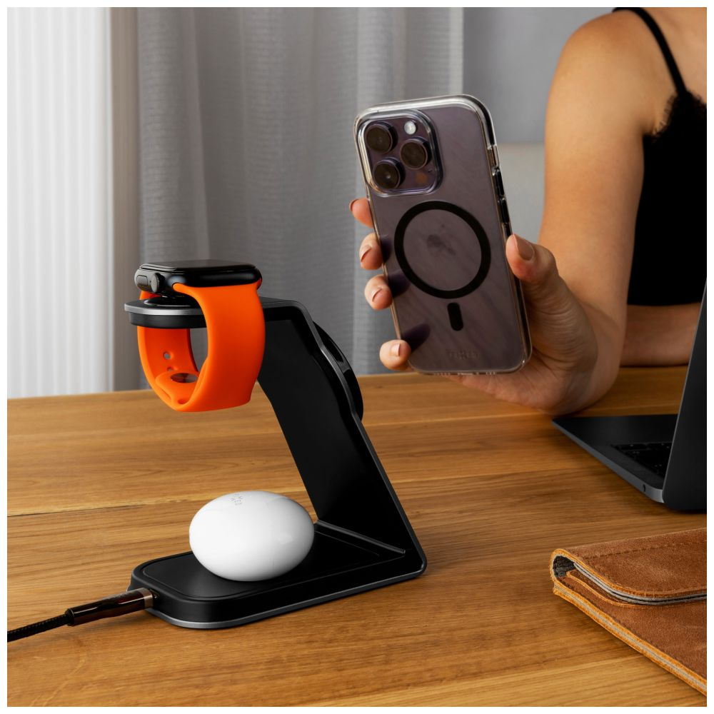 Eine orangefarbene Uhr und ein Telefon befinden sich auf einem schwarzen Ladeständer. Eine Person hält ein Telefon mit einer durchsichtigen Hülle.