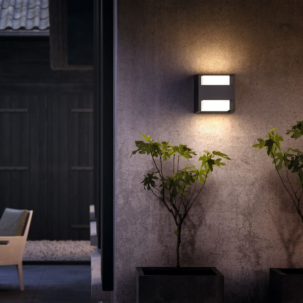 Una lámpara negra montada en la pared con dos luces, con plantas delante.