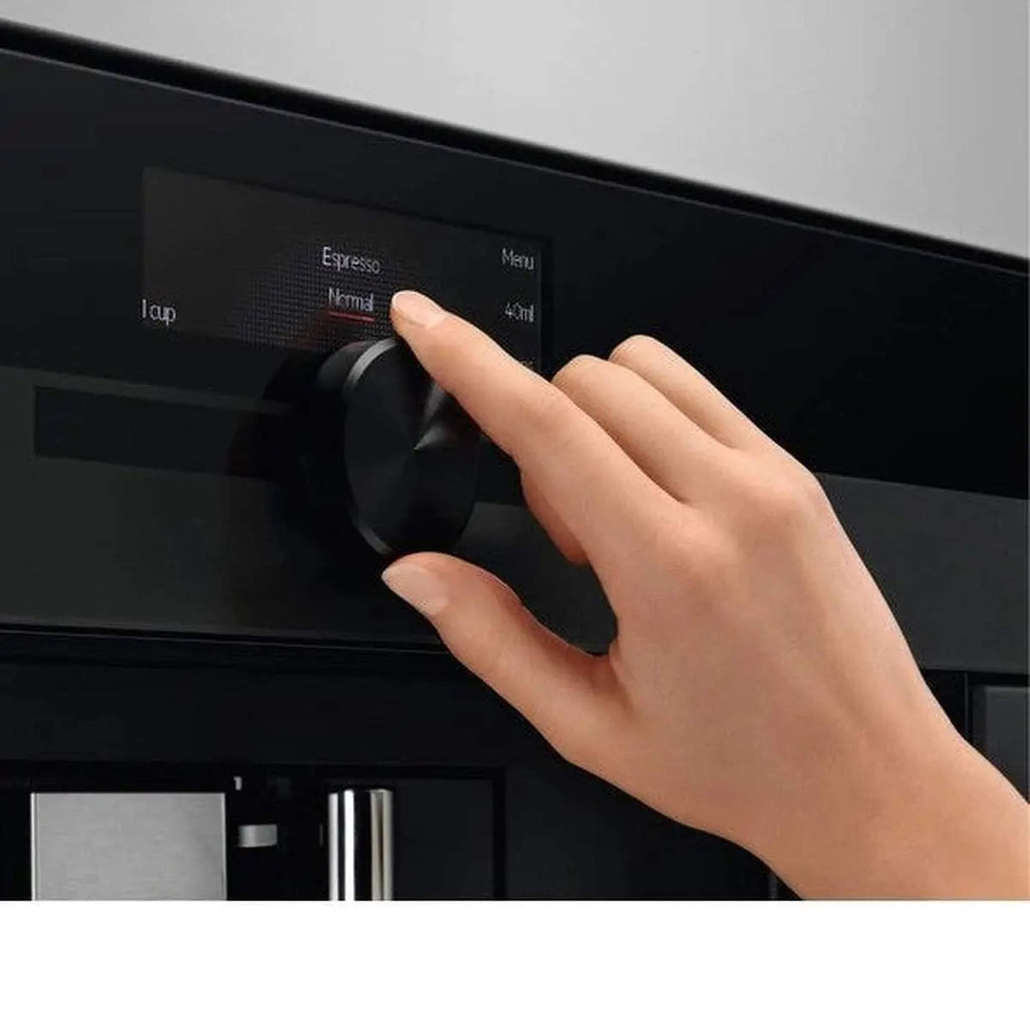 Una mano gira un dial negro en una cafetera negra, con una pantalla digital mostrando opciones.