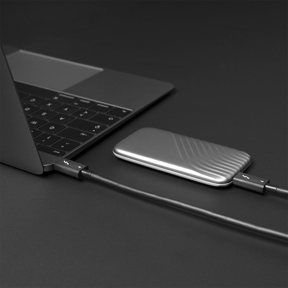 Laptop, zewnętrzny dysk SSD i czarny kabel Thunderbolt. Ciemna powierzchnia.