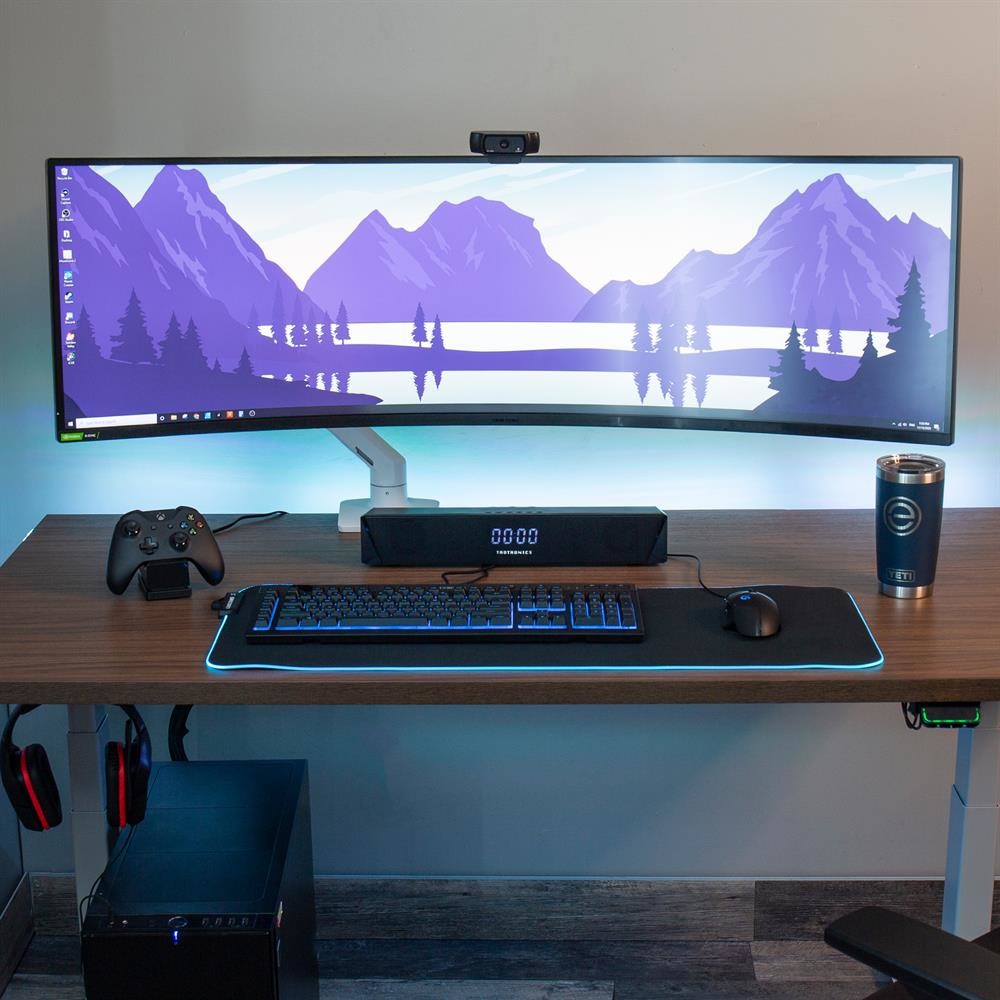 Configurazione gaming: monitor curvo, tastiera, mouse, altoparlanti, webcam, controller e bevanda.
