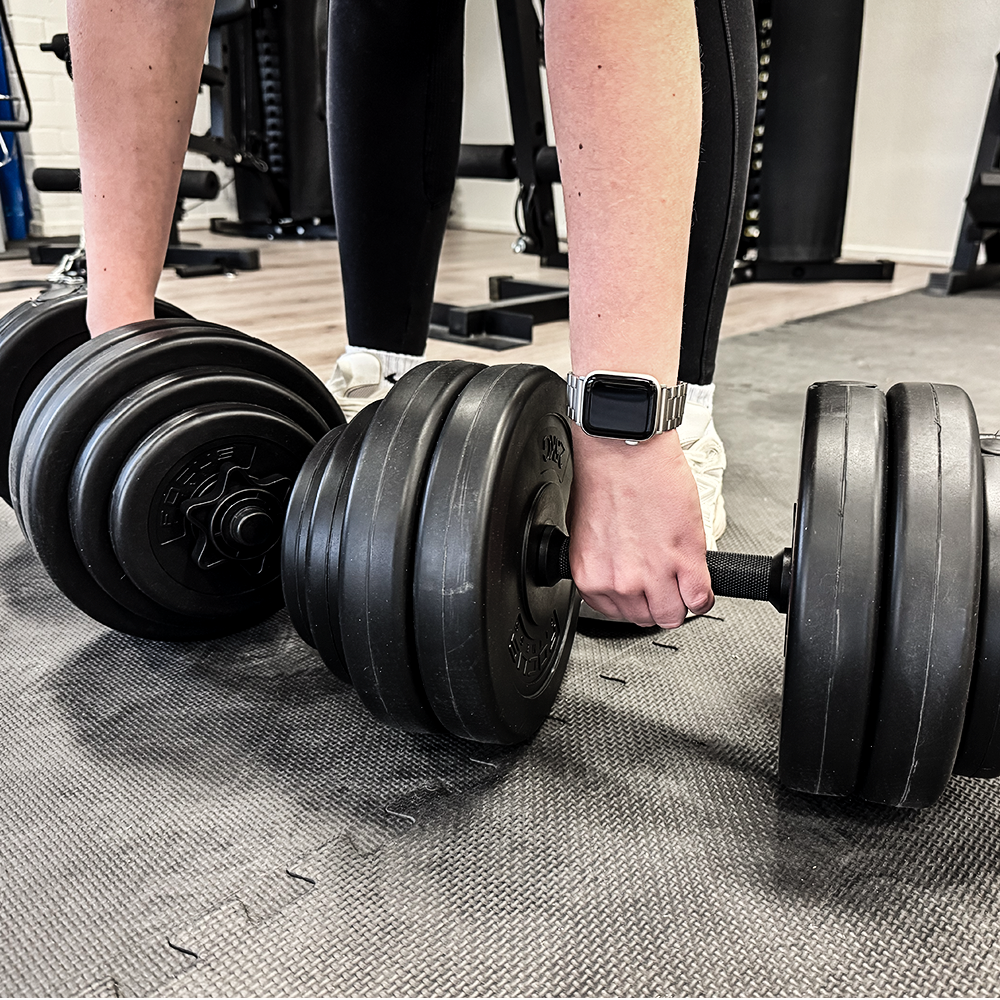 Person lifting two black dumbbells in a gym setting. 