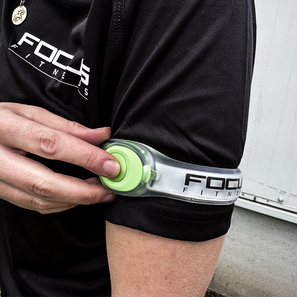 Een persoon met een zwart shirt doet een groene en doorzichtige armband om. Focus Fitness logo zichtbaar.