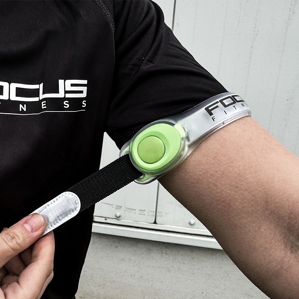 Persoon bevestigt een reflecterende armband met een groene knop en zwarte band.