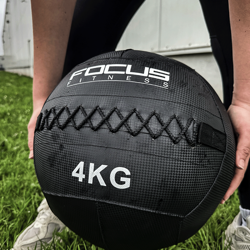 Une personne tenant un ballon médicinal noir. Le ballon a un logo Focus Fitness et le texte : 4KG.