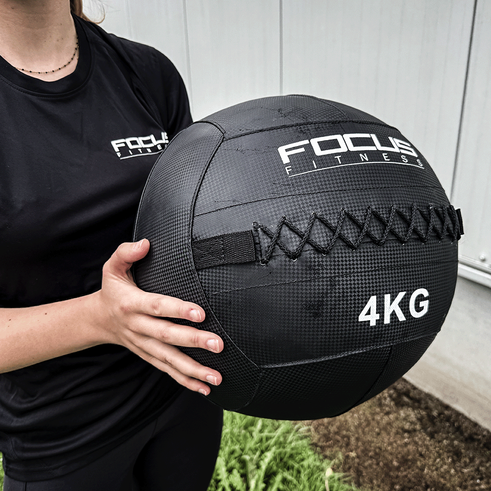 Une personne tenant un ballon médicinal Focus Fitness noir de 4 kg, logo visible.