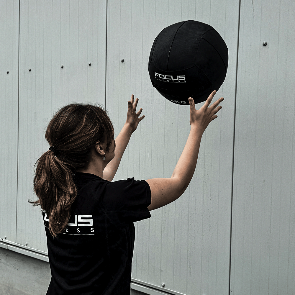 Femme lançant un ballon médicinal noir contre un mur.