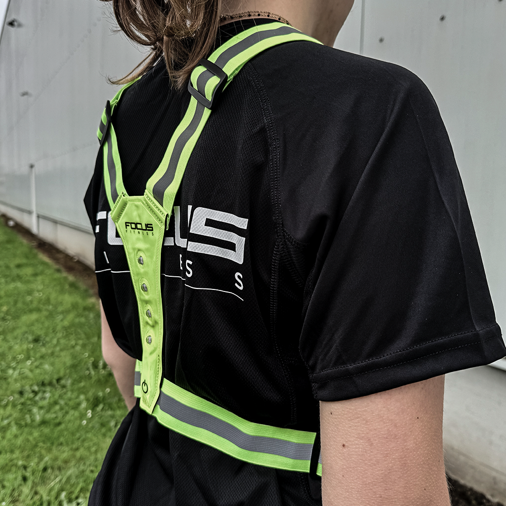 Een persoon met een zwart shirt en een reflecterend vest. Focus Fitness logo zichtbaar op het vest.