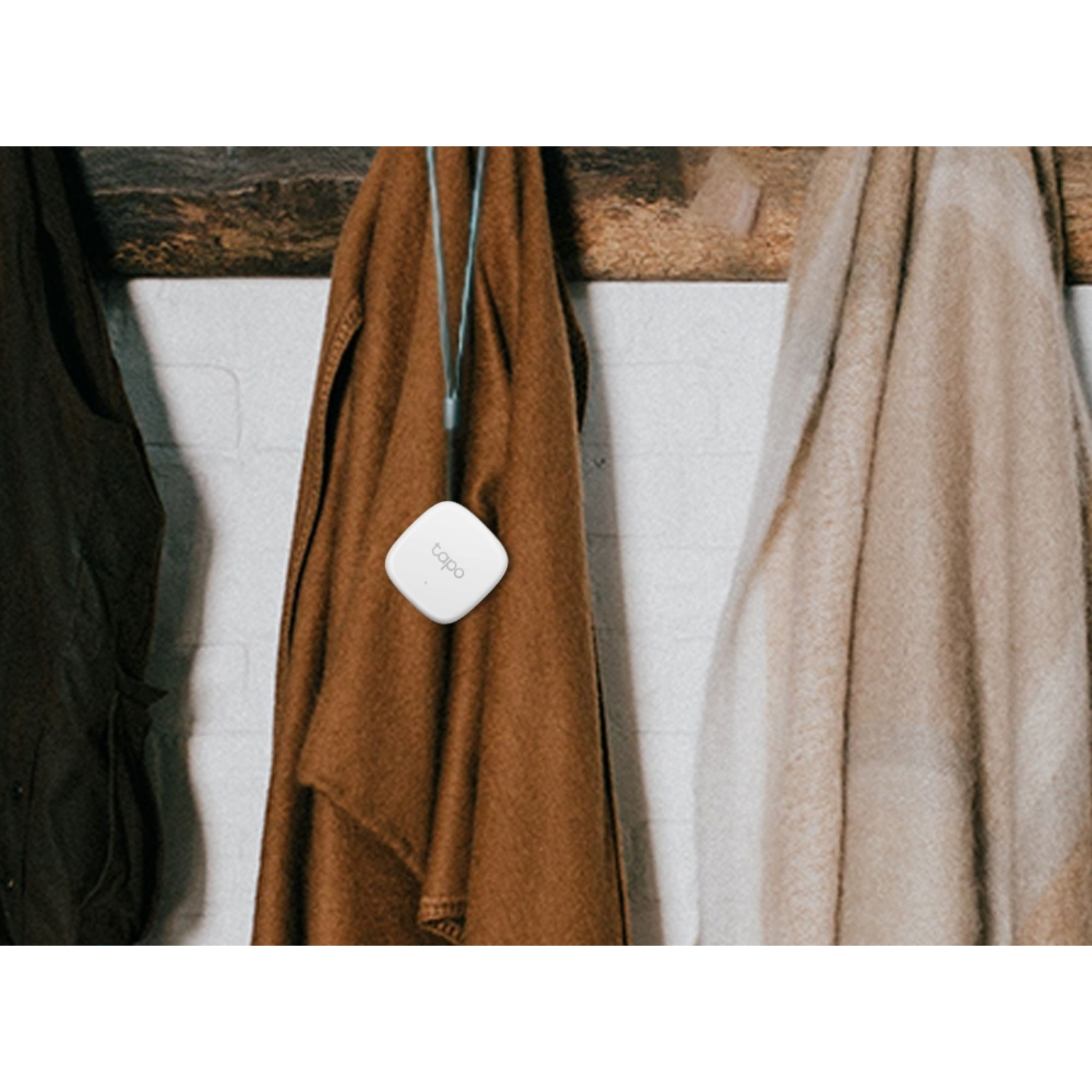 Ein weißes Tapo-Gerät, das an einer blauen Schnur an einer Garderobe hängt. Die Mäntel sind braun und beige.
