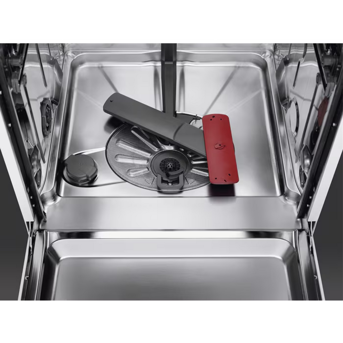 Wnętrze zmywarki ze stali nierdzewnej. Widoczny jest dolny kosz z obracającym się ramieniem i czerwonym elementem.