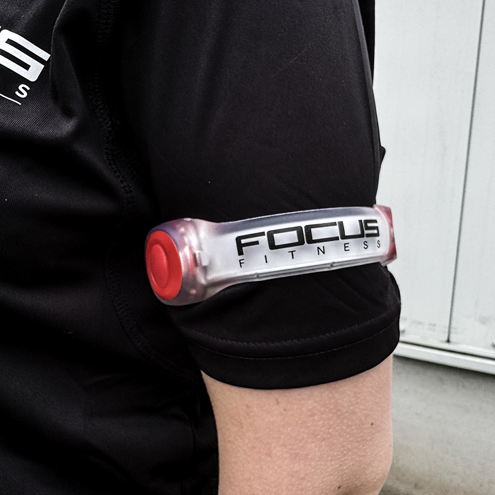 Persoon met zwart shirt heeft Focus Fitness band op bovenarm. Band is rood en doorschijnend.