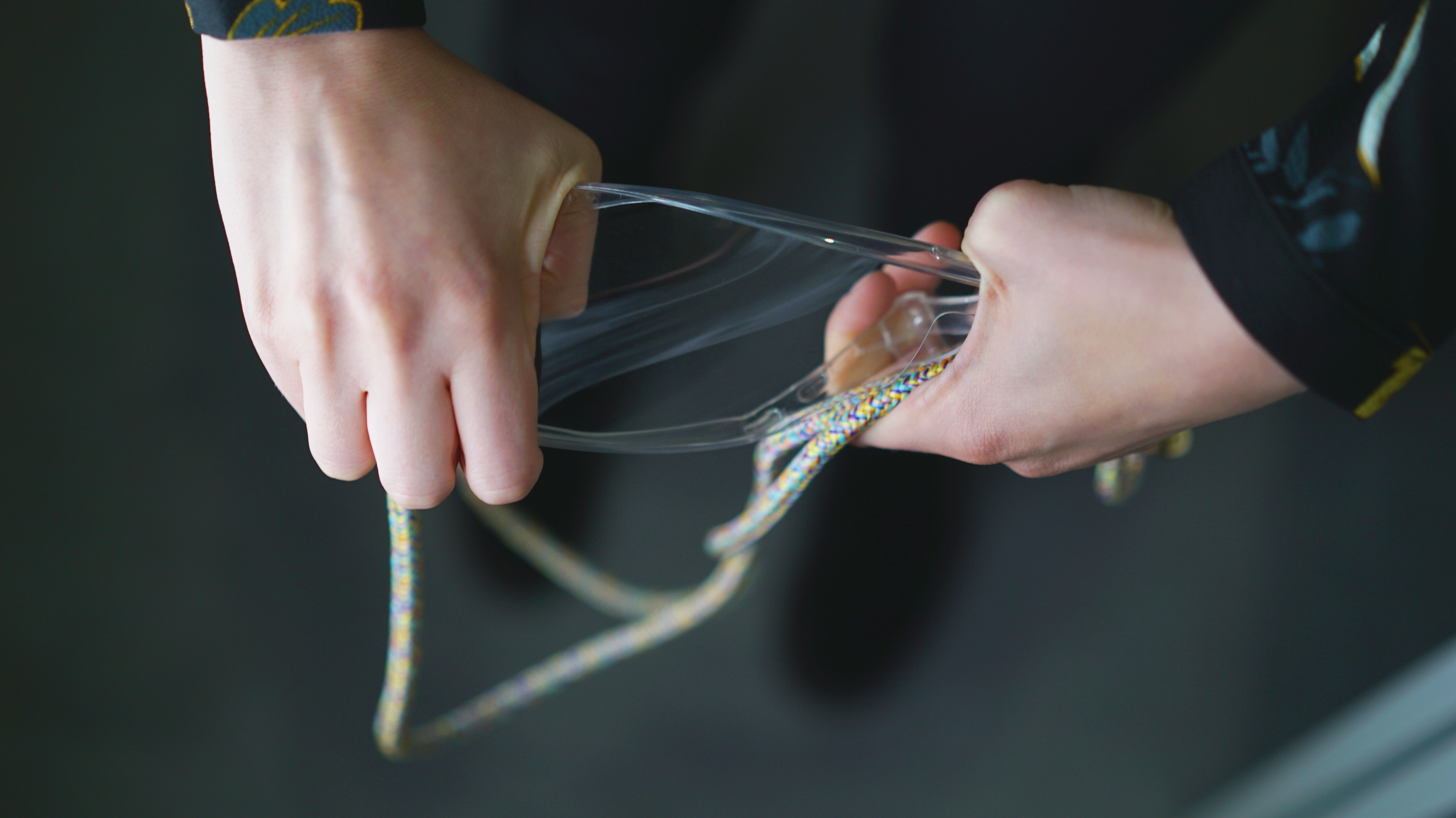 Hände halten eine transparente Handyhülle und ziehen sie auseinander. Ein Riemen ist ebenfalls befestigt.