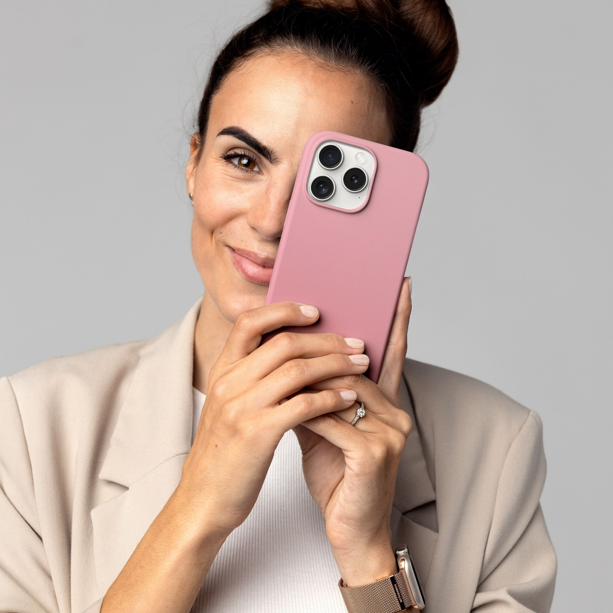 Frau hält pinkfarbene Handyhülle. Sie trägt einen beigen Blazer und hat ihr Haar zu einem Dutt gebunden.